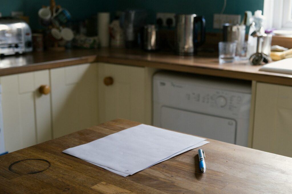 A blank sheet of paper and a pen on a kitchen table in a lived-in home.